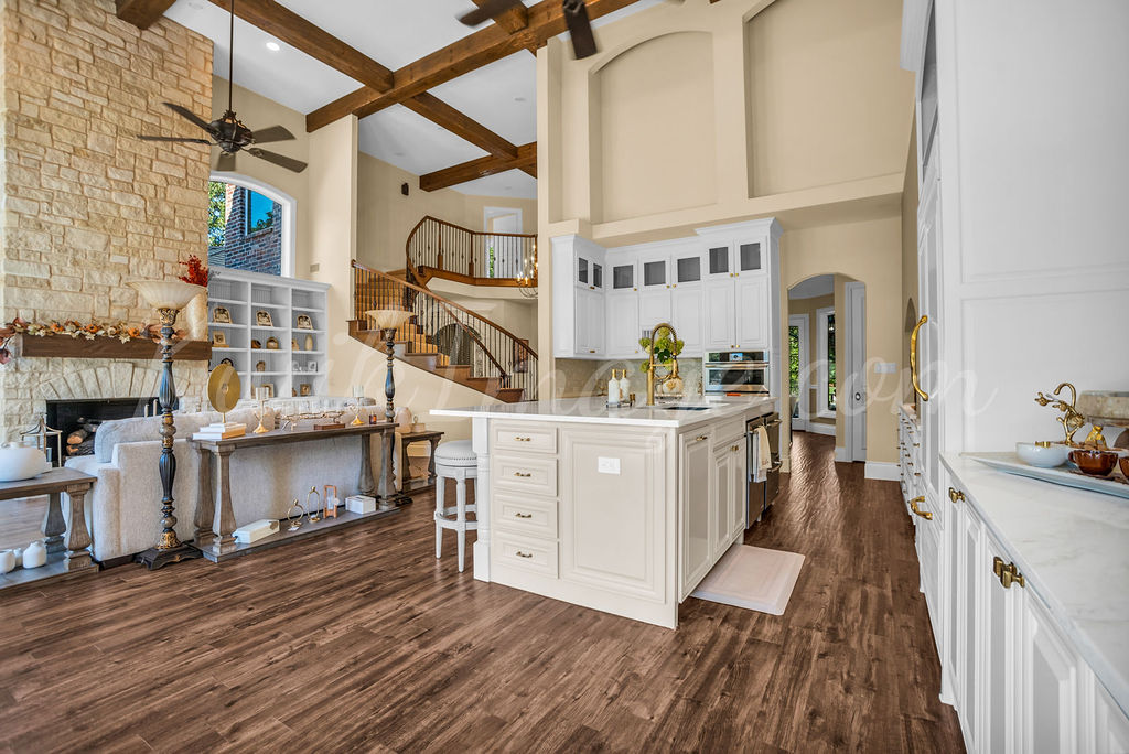 Open-plan kitchen with a white island, exposed wood beams and a stone fireplace